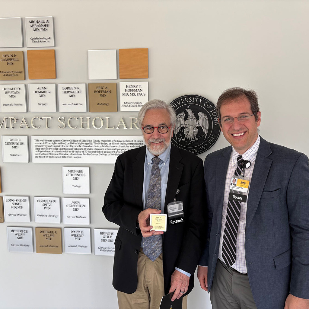 Eric Hoffman (holding plaque) and Bruno Policeni pose in front of Wall of Scholars in the Carver College of Medicine