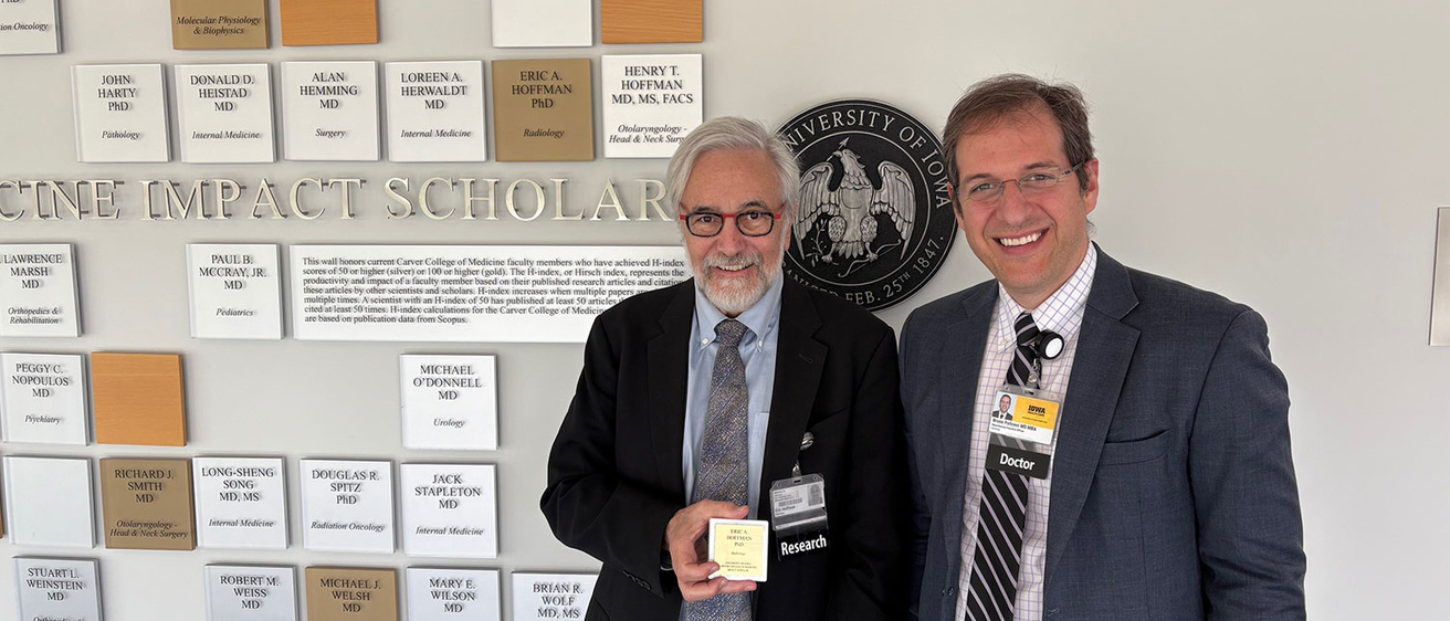 Eric Hoffman (holding plaque) and Bruno Policeni pose in front of Wall of Scholars in the Carver College of Medicine