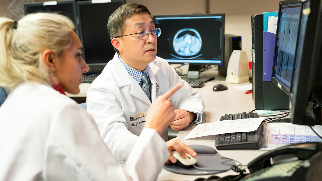 Faculty sitting with resident pointing at computer screen