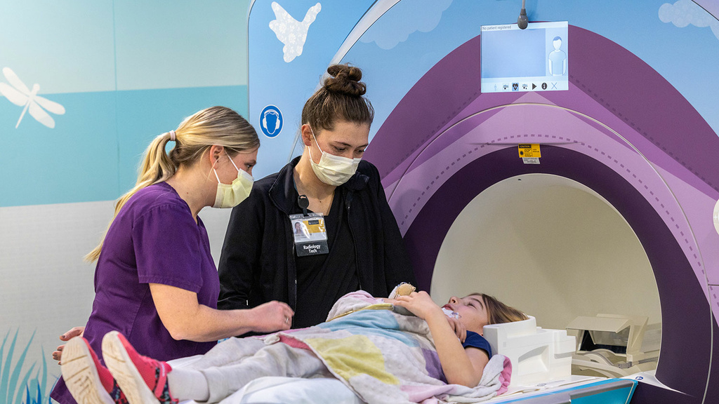 A radiology technologist and a mom talk to a child laying on a colorful MRI scanner bed