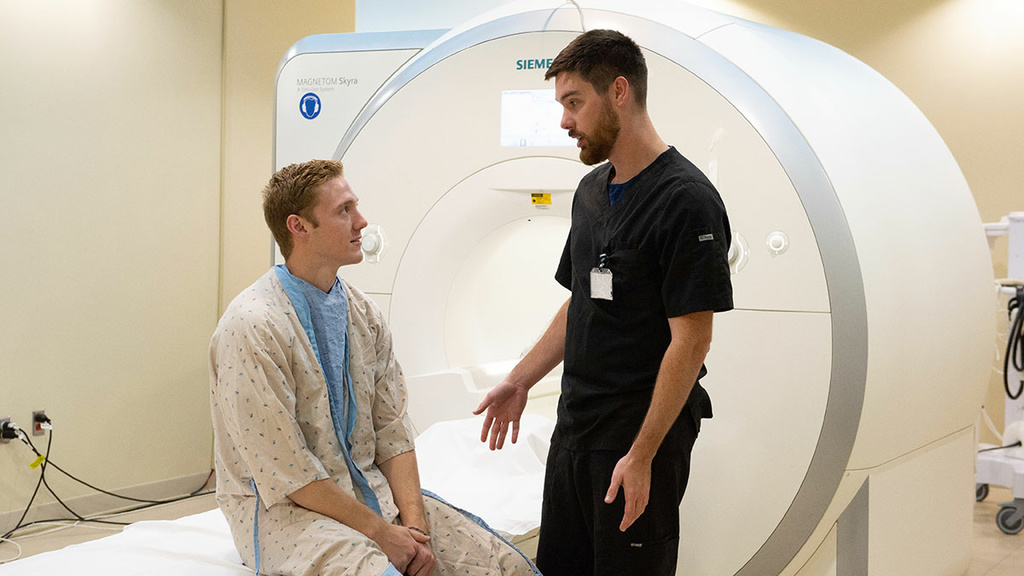 Rad tech speaks to patient sitting on a scanner bed