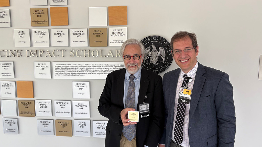 Eric Hoffman (holding plaque) and Bruno Policeni pose in front of Wall of Scholars in the Carver College of Medicine